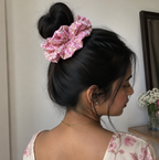 Woman with a pink scrunchie in her hair, wearing a floral top, in a room setting.