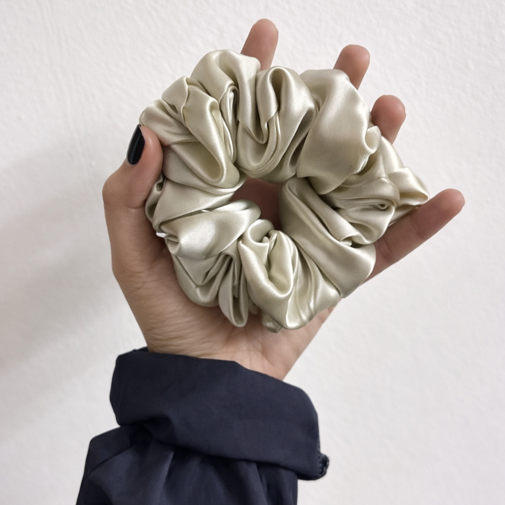 Hand holding a cream-colored scrunchie against a plain background