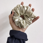 Hand holding a cream-colored scrunchie against a plain background